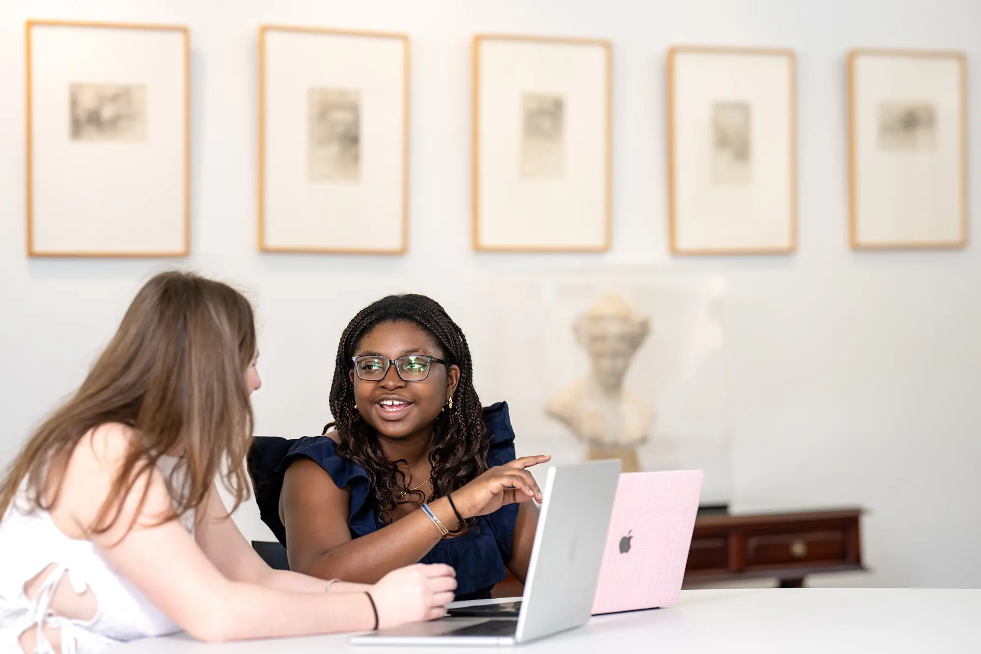 Two students sit at a table with laptops to study.