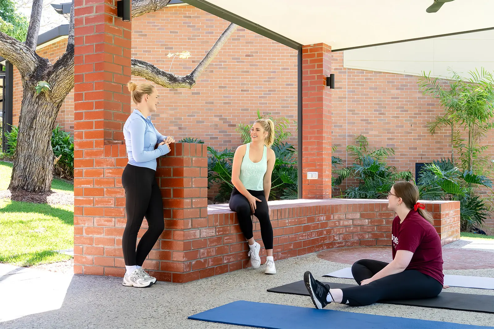 Three students participate in relaxation and recreation activities like yoga in an undercover area.