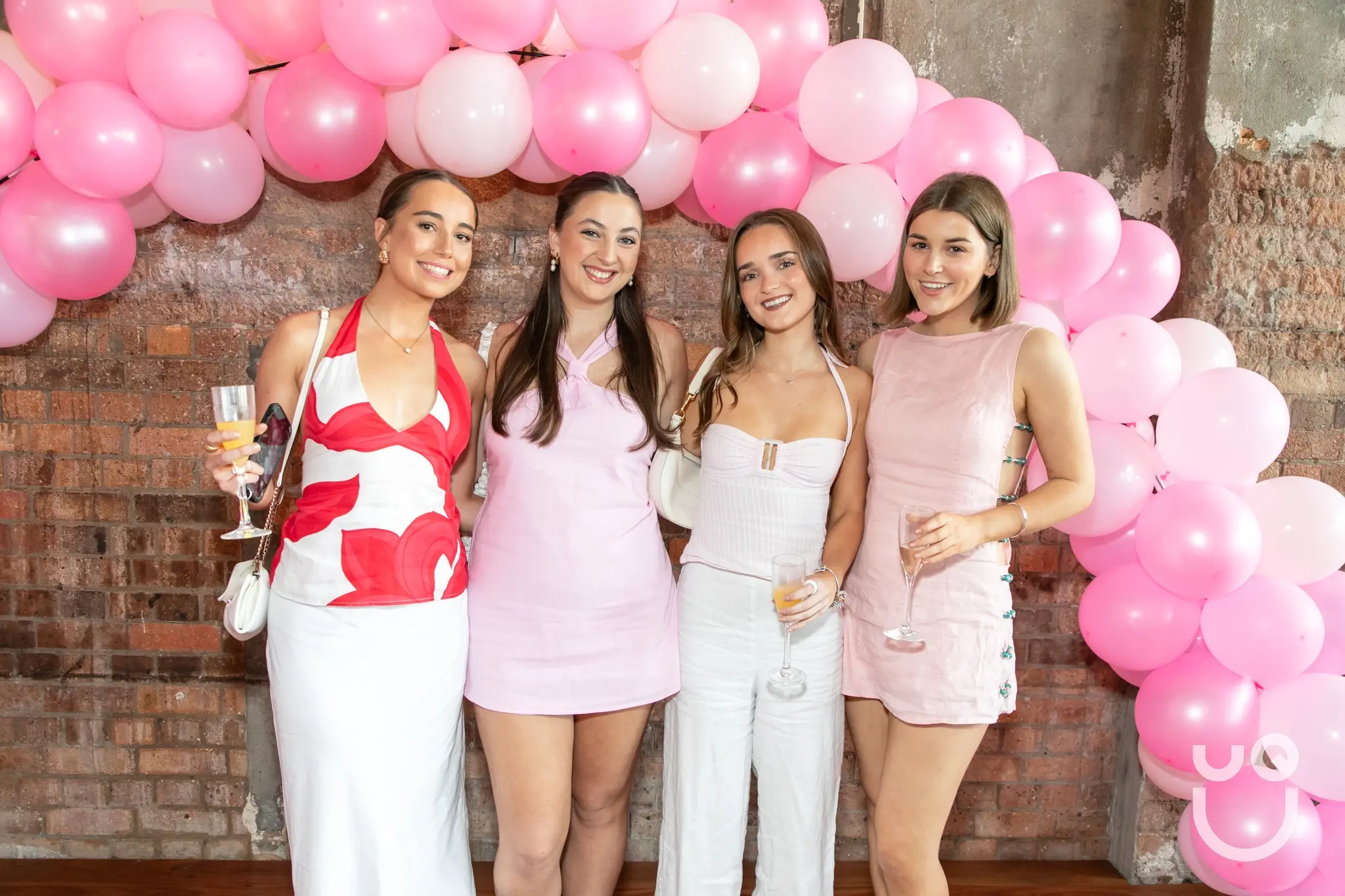 Four students wearing pink stand in front of a pink balloon arch.