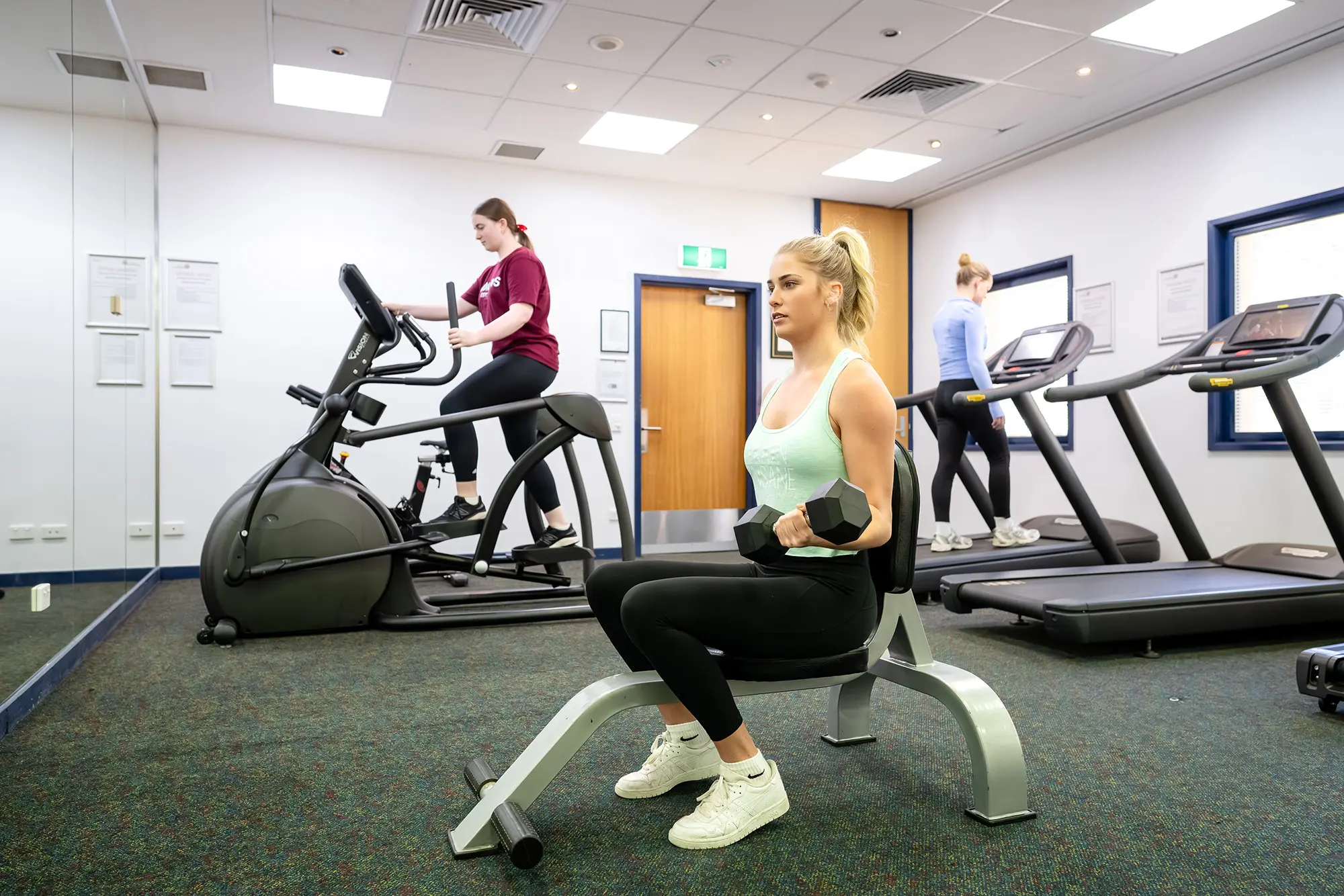 Students work out in a gym that features treadmills, stepping machines, and weight-lifting equipment.
