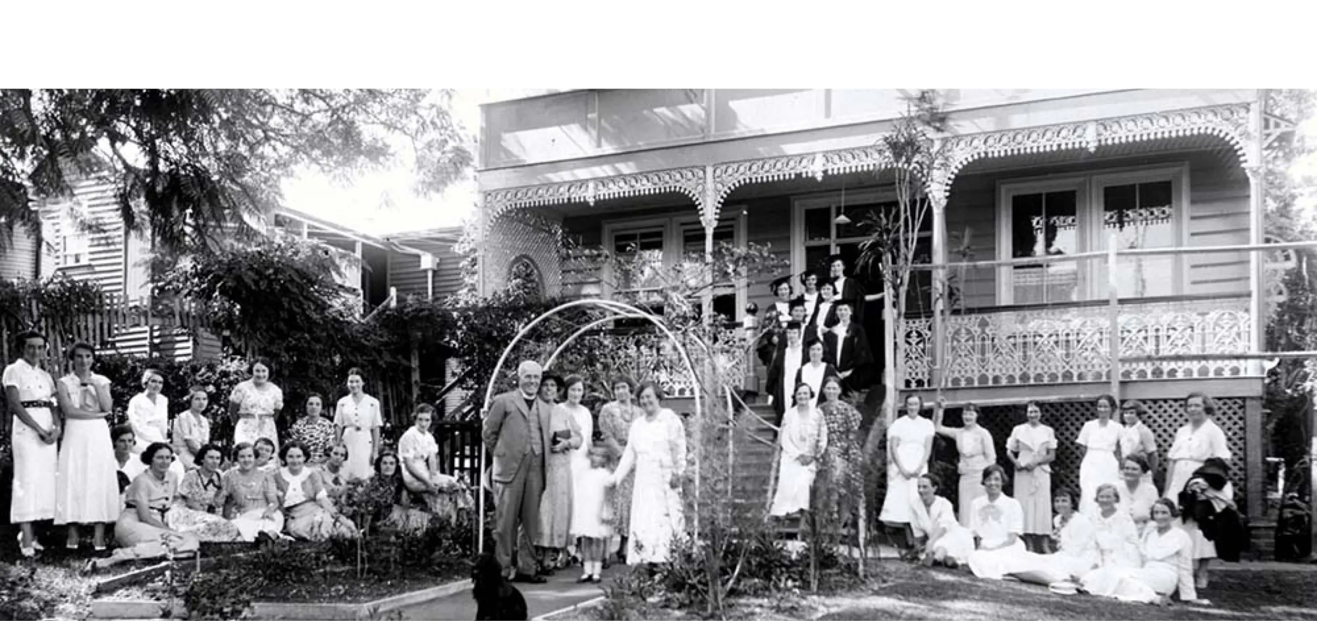 A black and white photo of a group of people standing in front of a Queenslander-style home.