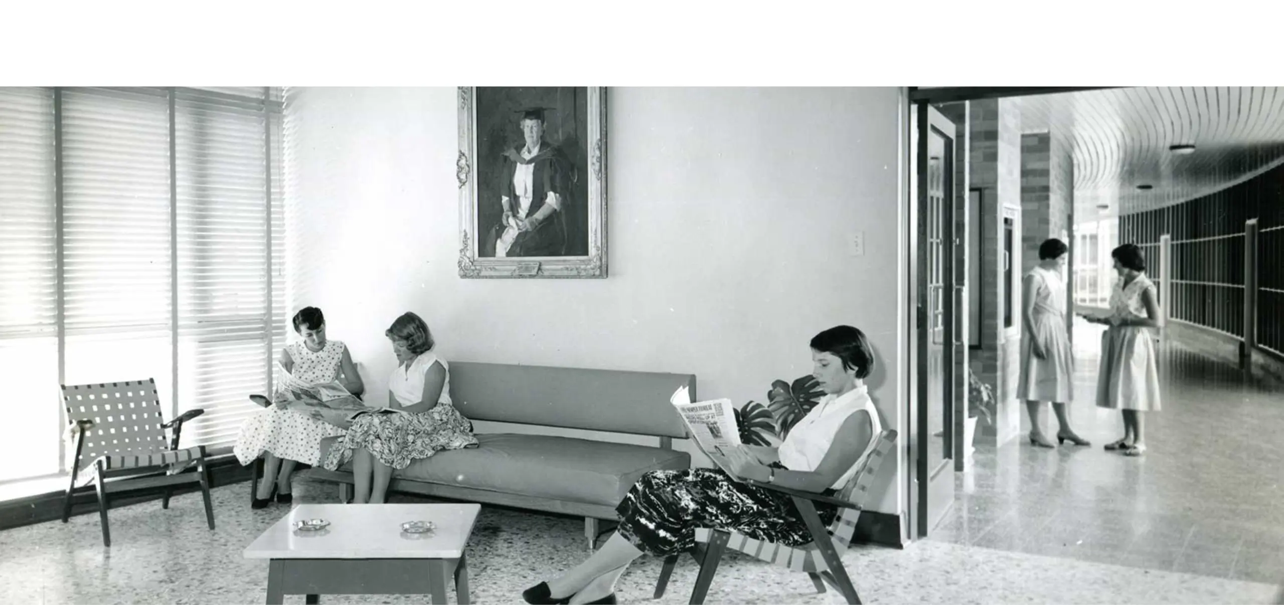 A black and white photo of two students sitting in chairs and reading in a foyer.