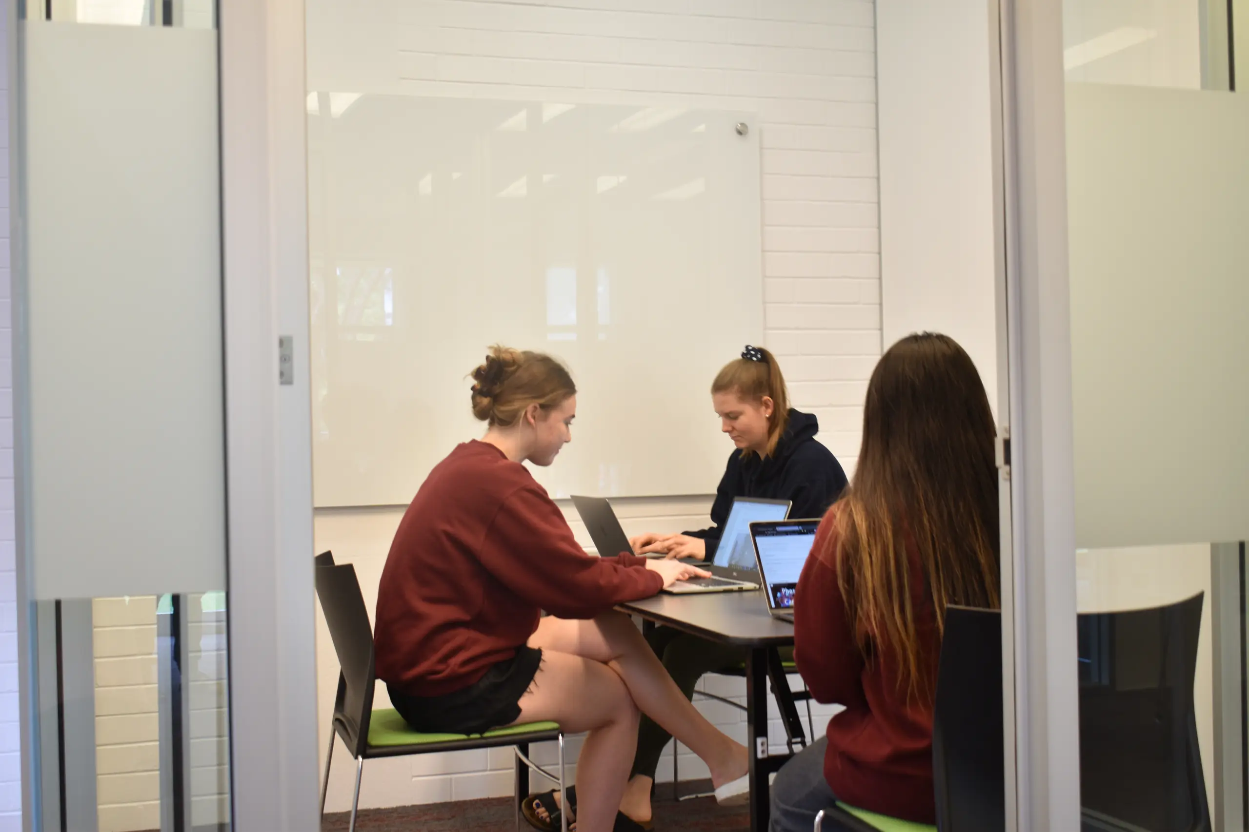 Three students seated around a table and studying on their laptops.