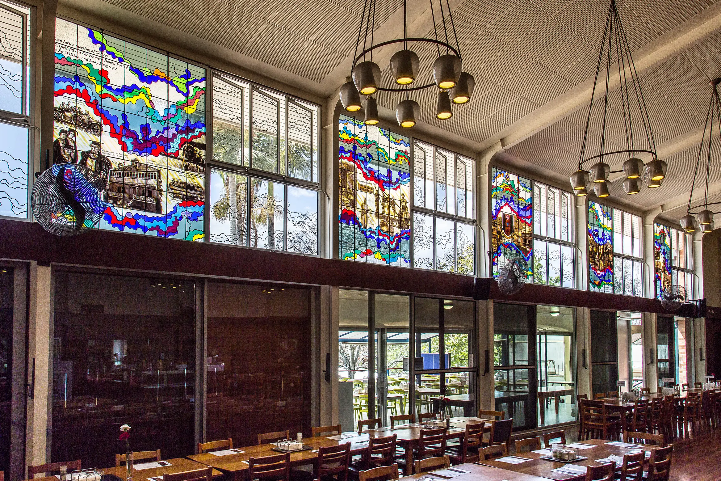 Inside a dining hall, looking up at five stained-glass window panels.