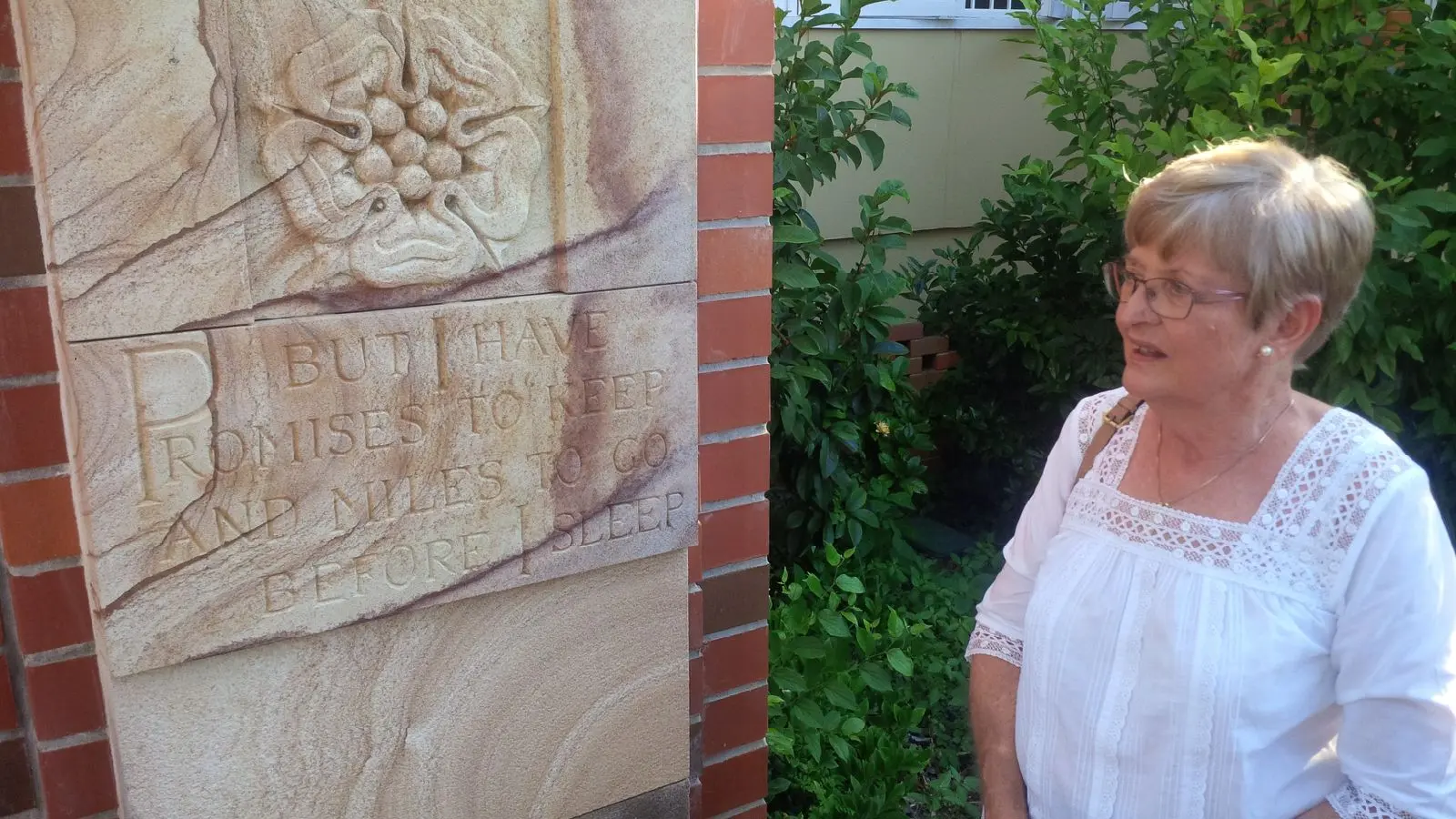 A woman in a white shirt stands next to an engraved sandstone sculpture.