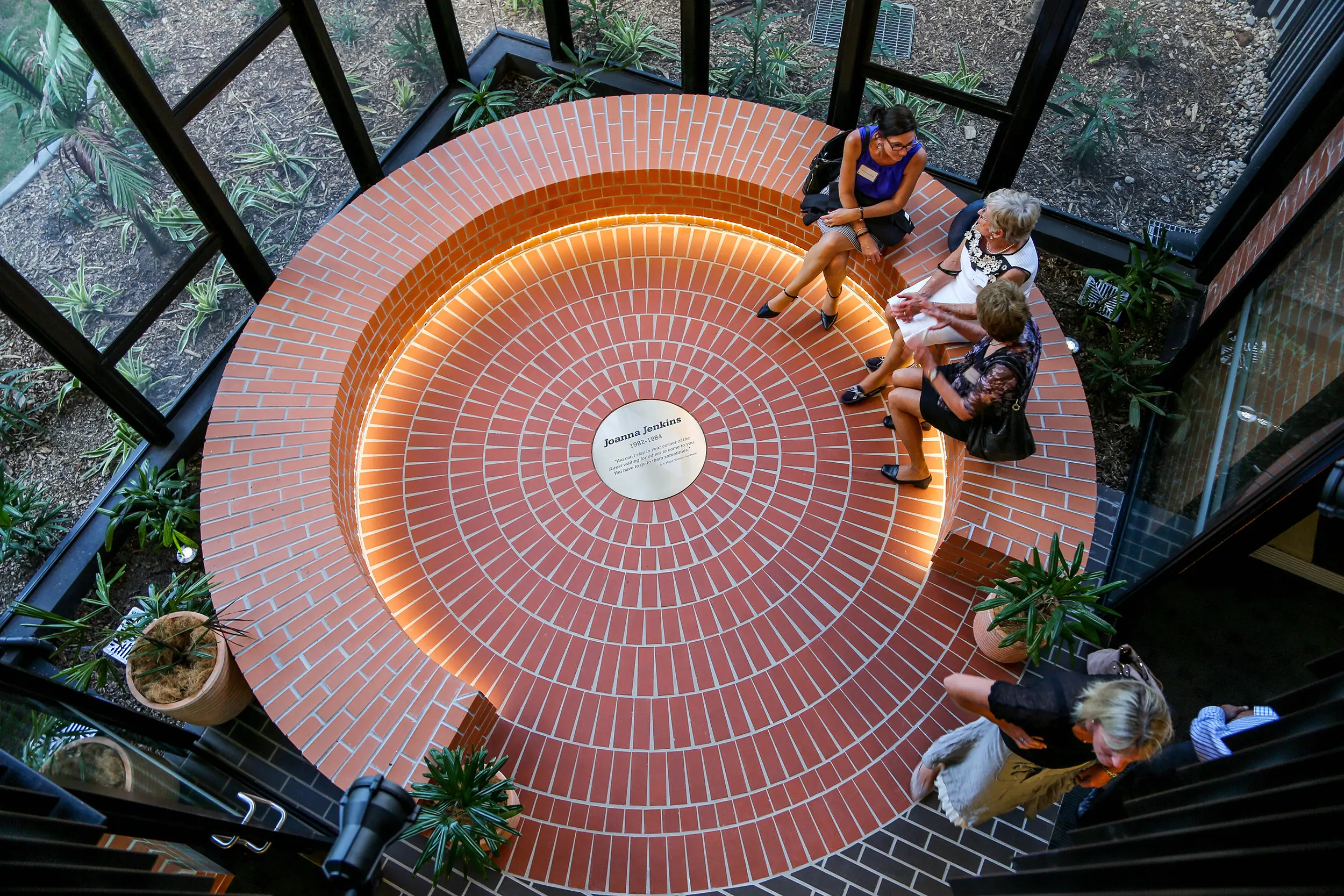 An overhead photo of a red brick circle with a few people seated on the brick bench.