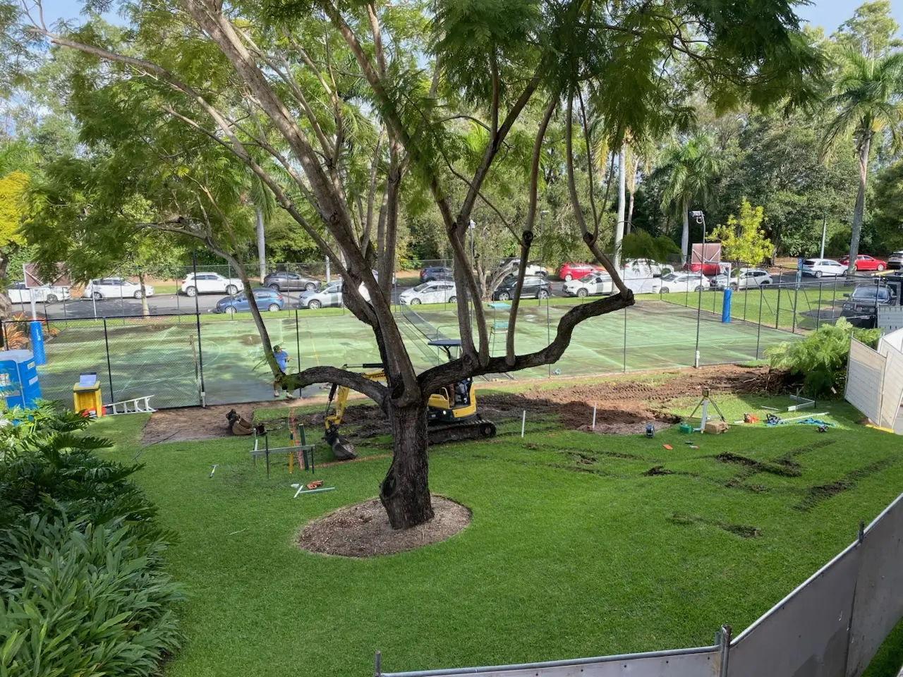 A construction site on a grassy area in front of a tennis court.
